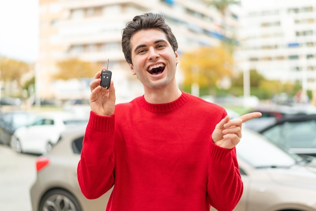 Young handsome man with car key surprised and pointing finger to the side