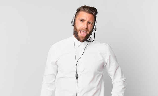 Young handsome man with cheerful and rebellious attitude, joking and sticking tongue out. telemarketing concept