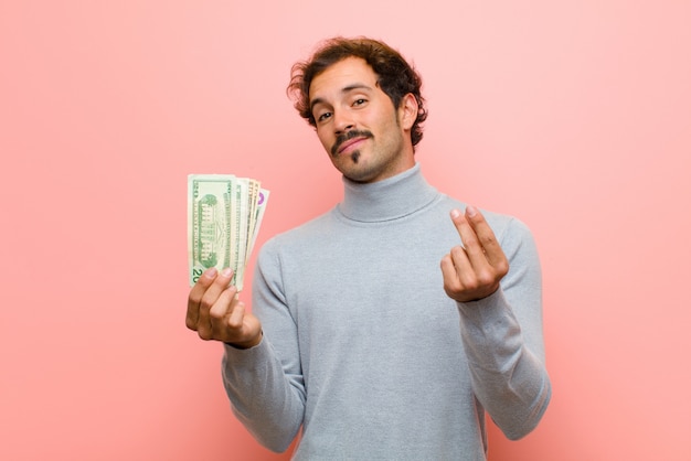 Young handsome man with dollar banknotes on pink flat wall