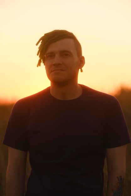 Young handsome man with dreadlocks posing against sky on sunset