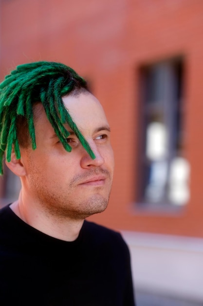 Young handsome man with green dreadlocks in black tshirt posing on city street