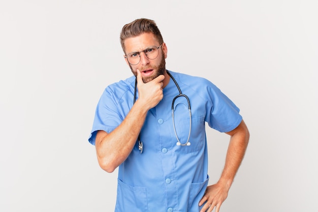 Young handsome man with mouth and eyes wide open and hand on chin. nurse concept