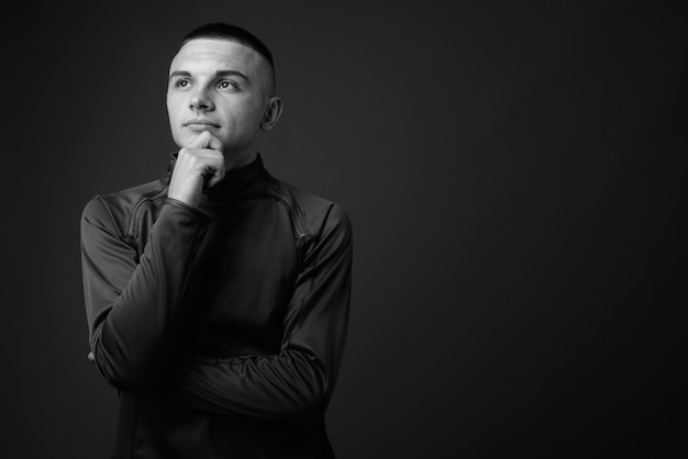 young handsome man with short hair wearing high collar shirt against gray wall. black and white