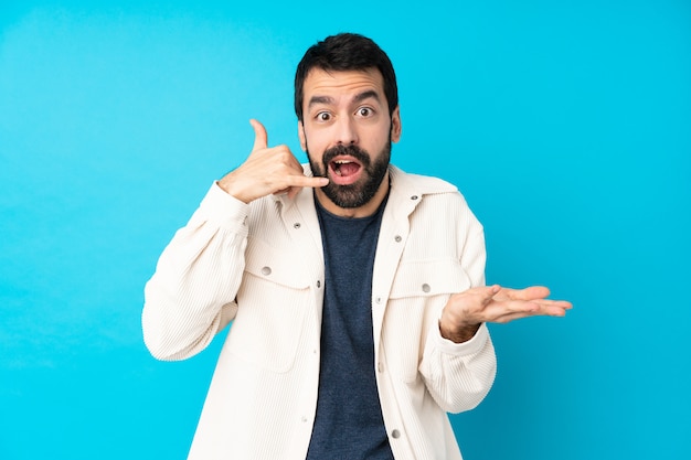 Young handsome man with white corduroy jacket over isolated blue wall making phone gesture and doubting