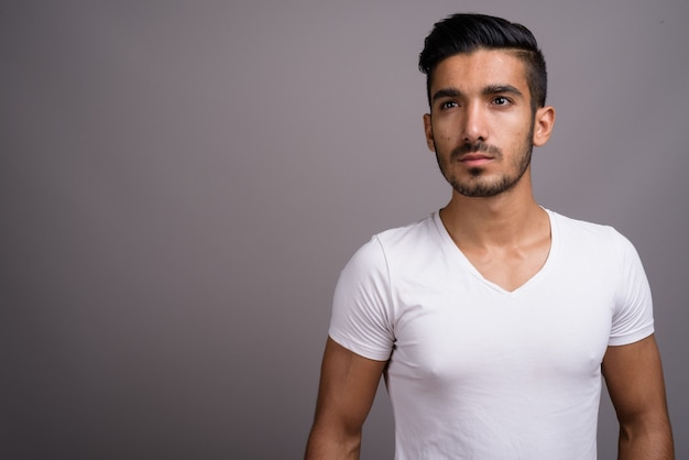 Young handsome Persian man against gray background