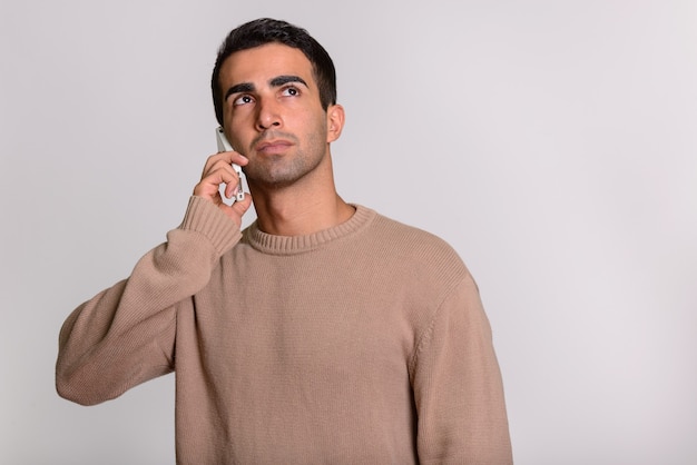 Young handsome Persian man talking on phone while thinking