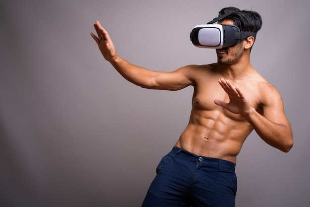 Young handsome Persian man using virtual reality headset shirtless