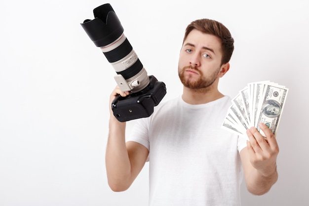 Young handsome photographer with a beard in a white shirt holding a camera and hundred dollar bills. payment for the photo shoot