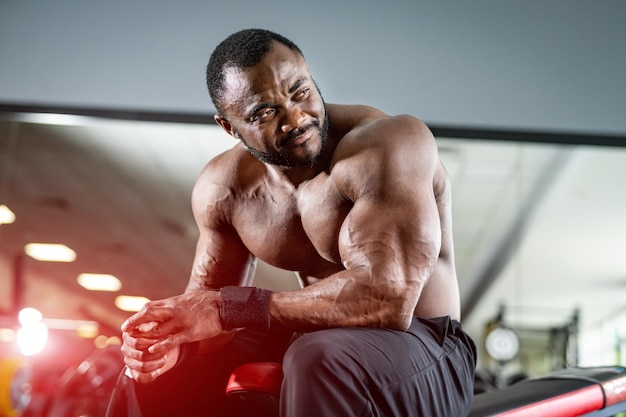 Young handsome sportsman with nice body Multiracial fitness male sitting at the bench and looking away Gym background Naked torso Blurred background