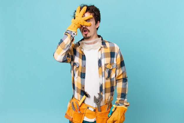 Young handyman housekeeper looking shocked, scared or terrified, covering face with hand