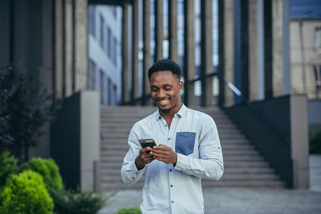 Young happy african american male freelancer corresponding in mobile and reading good news from mobile phone online