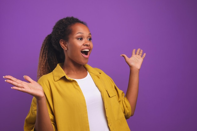 Young happy african american woman opens mouth and spreads arms to sides