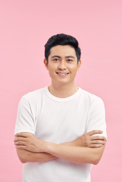 young happy asian man standing with arms crossed over pink wall. Looking at camera.