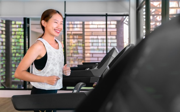 Young happy asian woman athlete run on treadmill running machine in indoor gym fitness for health