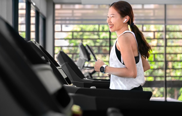 Young happy asian woman athlete run on treadmill running machine in indoor gym fitness for health