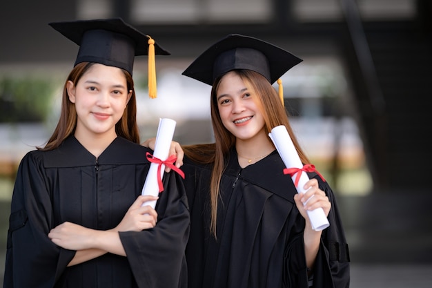 Young happy Asian woman university graduates in graduation gown and mortarboard hold a degree certificate celebrate education achievement in the university campus.  Education stock photo