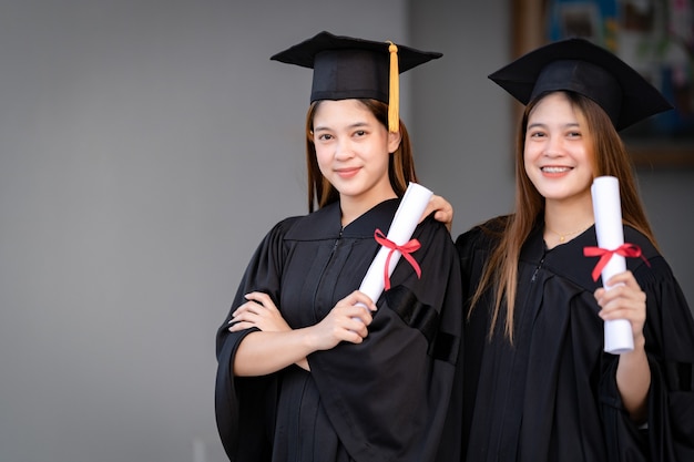 Young happy Asian woman university graduates in graduation gown and mortarboard hold a degree certificate celebrate education achievement in the university campus.  Education stock photo