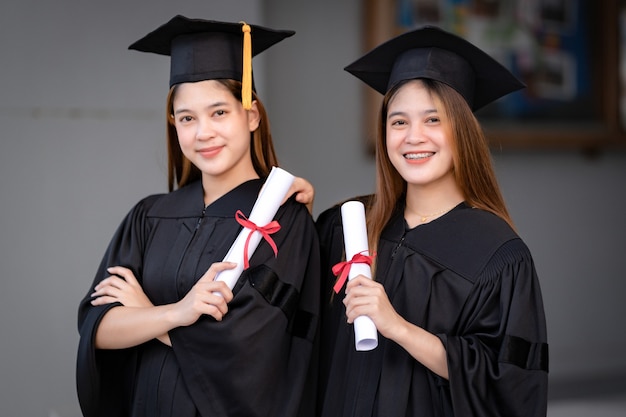 Young happy Asian woman university graduates in graduation gown and mortarboard hold a degree certificate celebrate education achievement in the university campus.  Education stock photo