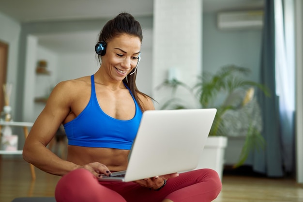 Young happy athletic woman using computer while relaxing on the floor in the living room