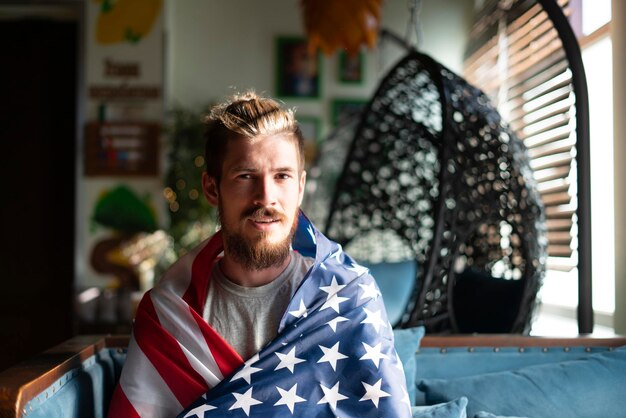 A young happy bearded guy covered with usa american flag