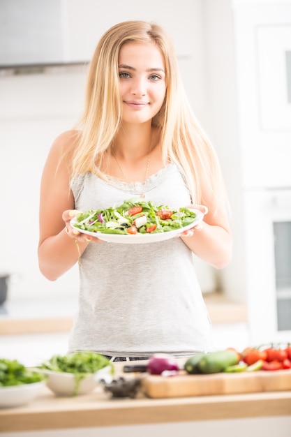 Young happy blonde girl eating healthy salad from arugula spinach tomatoes olives onion and olive oil.