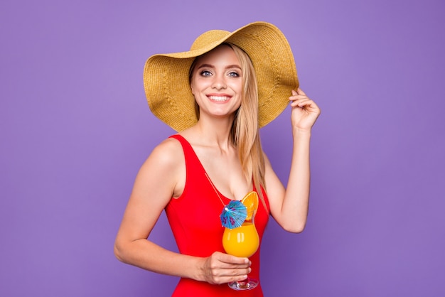 Young happy blonde girl holding cold summer cocktail in hand isolated on purple