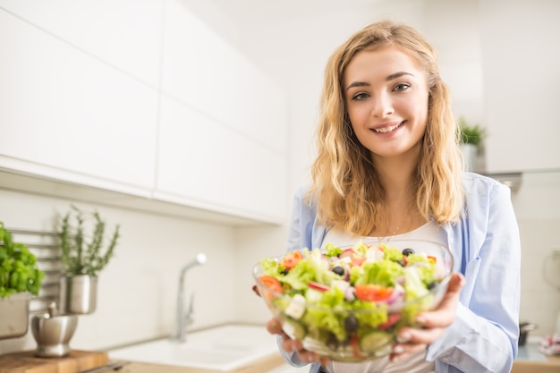 Young happy blonde girl preparing healthy salad in home kitchen.