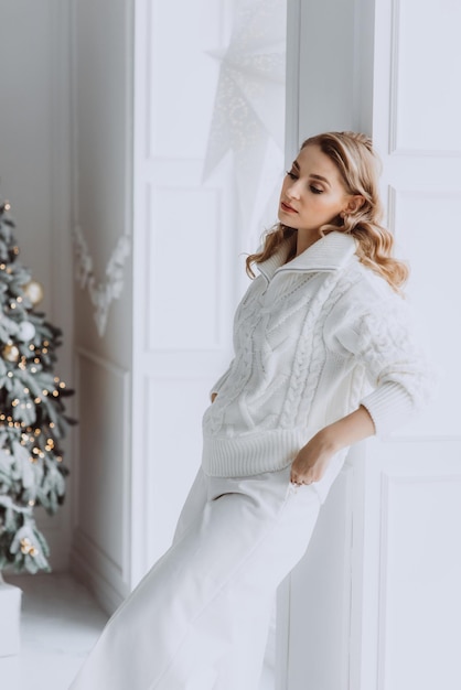 Young happy blonde woman in white clothes on the background of a Christmas tree Soft selective focus