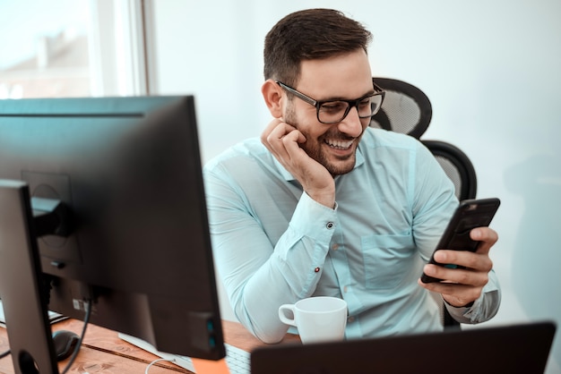 Young happy businessman smiling while reading message on his smartphone.