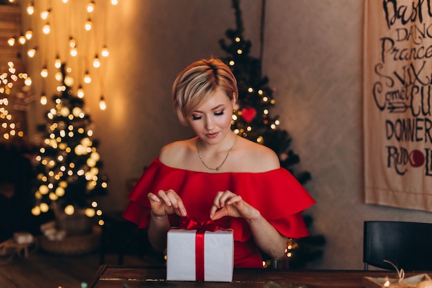 Young happy cheerful woman in red dress with new year present box in hands in christmas decorated home. Christmas, happiness,beauty, presents concept