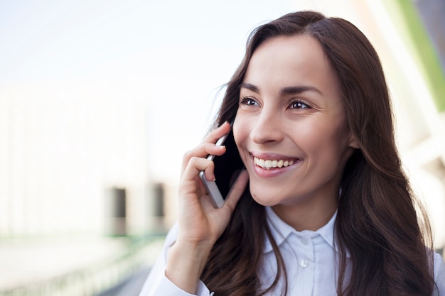 Young happy confident business woman is using her smartphone while walking outdoors in an urban city