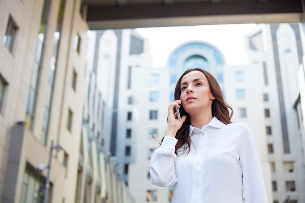 Young happy confident business woman is using her smartphone while walking outdoors in an urban city