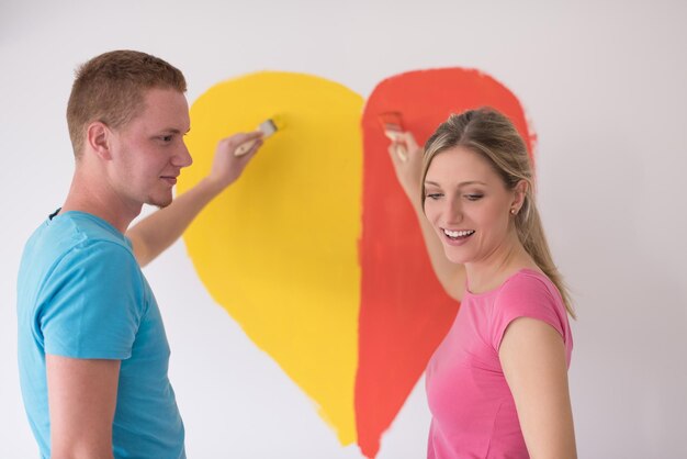 Young happy couple are painting a heart on the wall while doing repair at home.