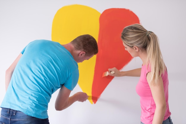 Young happy couple are painting a heart on the wall while doing repair at home.