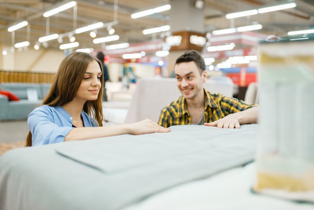 Young happy couple buying blanket for bed in furniture store. 