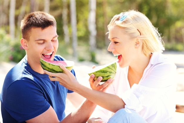 a young happy couple eating watermelon at the beach