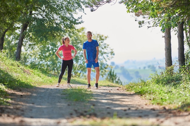 young happy couple enjoying in a healthy lifestyle while jogging on a country road through the beautiful sunny forest, exercise and fitness concept