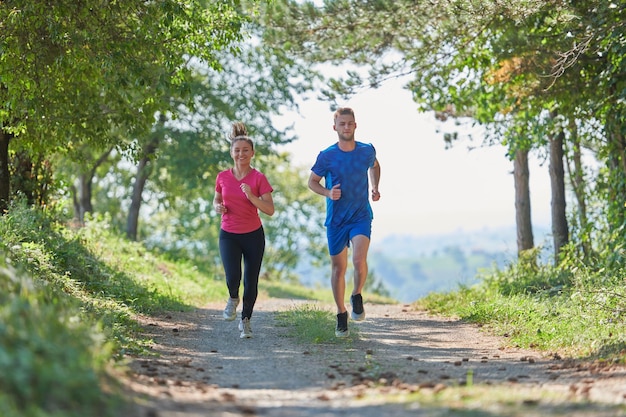 young happy couple enjoying in a healthy lifestyle while jogging on a country road through the beautiful sunny forest, exercise and fitness concept