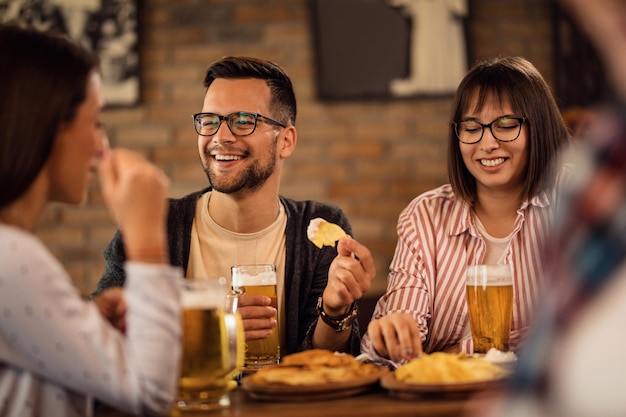 Young happy couple enjoying with friends while drinking beer and having a snack in a tavern