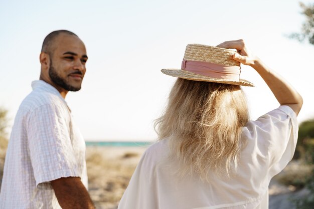 Young happy couple holding hands and walking together to the beach on summer day