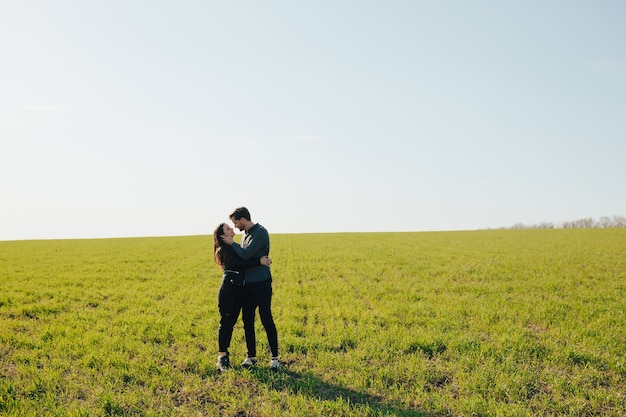 Young happy couple hugging on a green meadow with blue sky on the background.