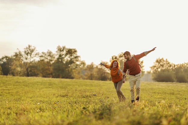 Young happy couple in love holding hands and running on meadow. It's a beautiful sunny autumn day.