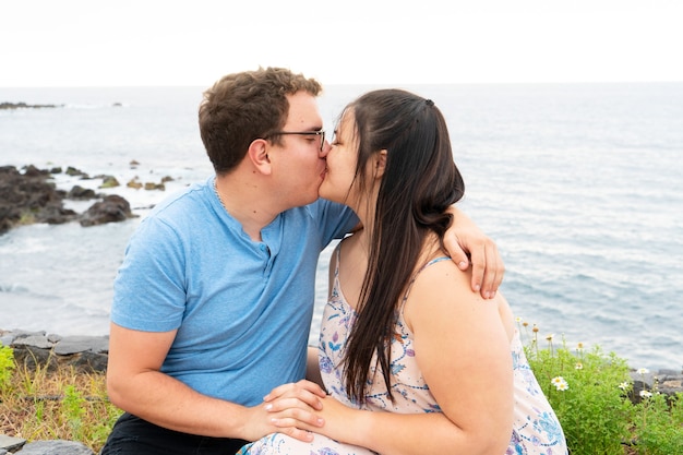 Young happy couple in love kissing each other and embracing while dating on seaside on summer day, man and woman smiling with eyes closed while enjoying intimate moment outdoors