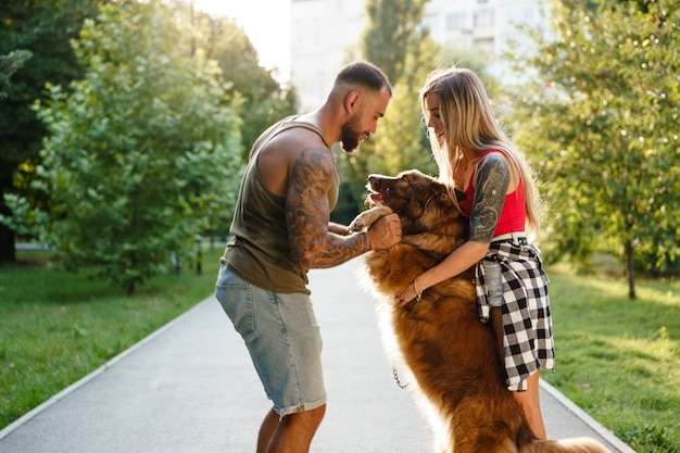 Young happy couple playing with their dog smiling in park