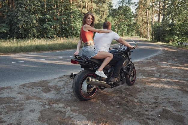 A young happy couple rides a motorcycle on an asphalt road in the forest freedom and travel in motio