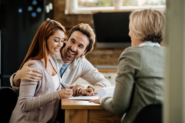 Young happy couple signing lease agreement while having a meeting with real estate agent at home.