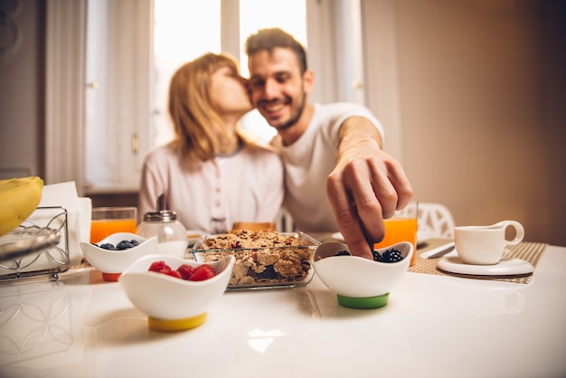 Young happy couple sitting by table having breakfast together at morning. Focus on the hand.