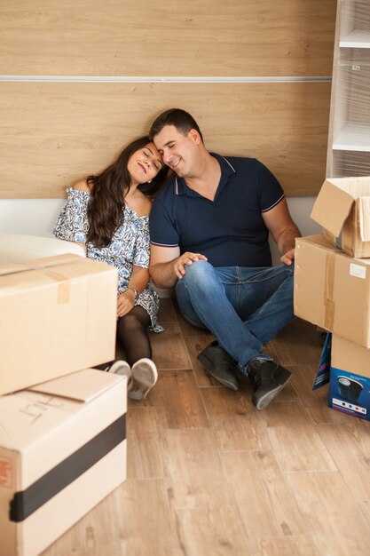 Young happy couple sitting on the floor resting after unpacking. Couple chilling after carrying boxes