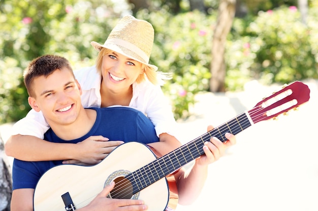 young happy couple sitting together on the beach and playing guitar