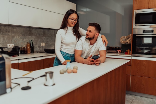 Young happy couple using two phones share social media news at home smiling husband and wife millennial users customers talking doing shopping online sit at table mobile tech lifestyle concept